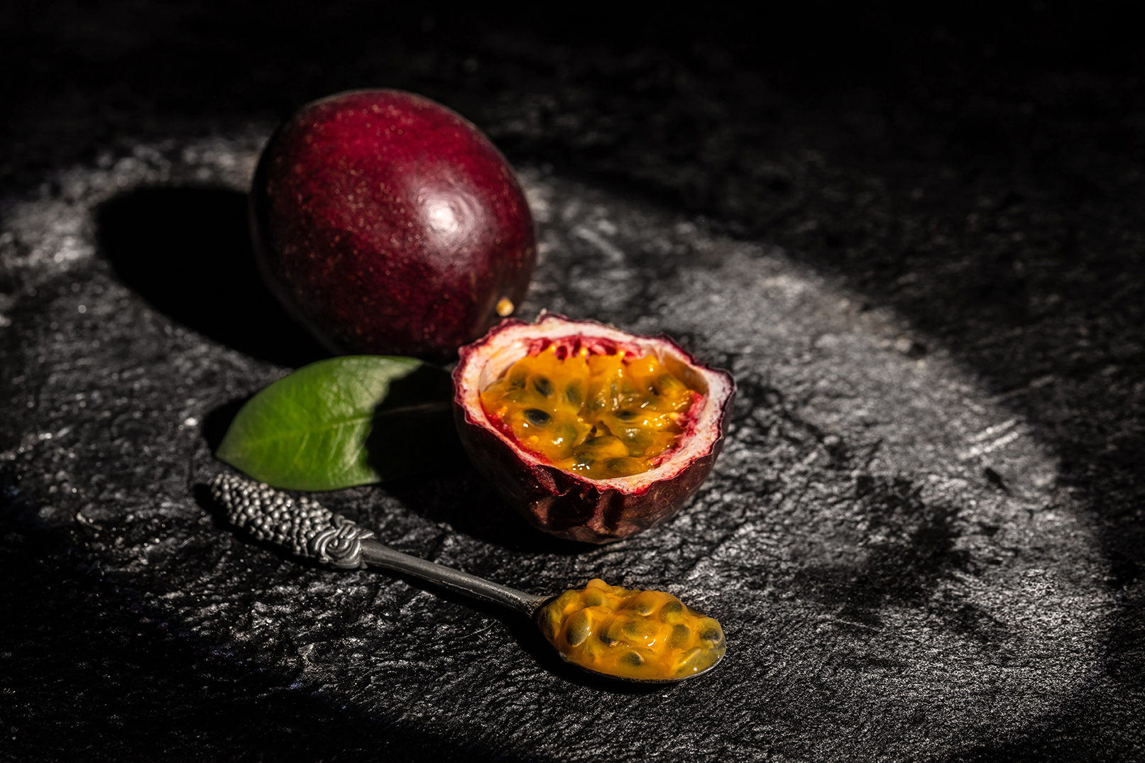 Sliced & whole passion fruit next to a spoon containing some of the fruit