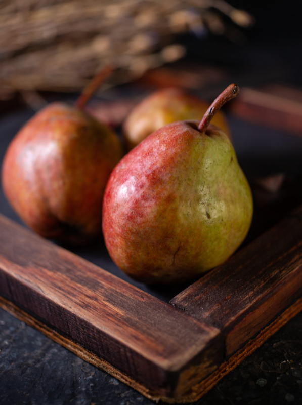 Autumn pears on the dark rustic background | Purée Arêté Two ripe pears resting on a wooden tray on a dark surface.
